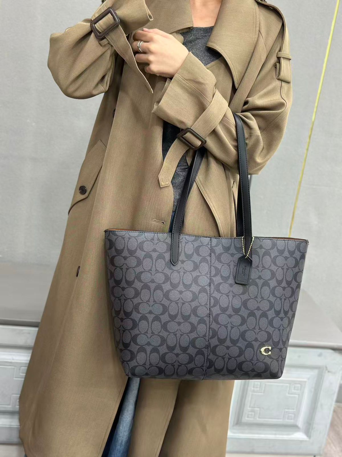 Model carrying black Coach signature canvas leather tote bag
