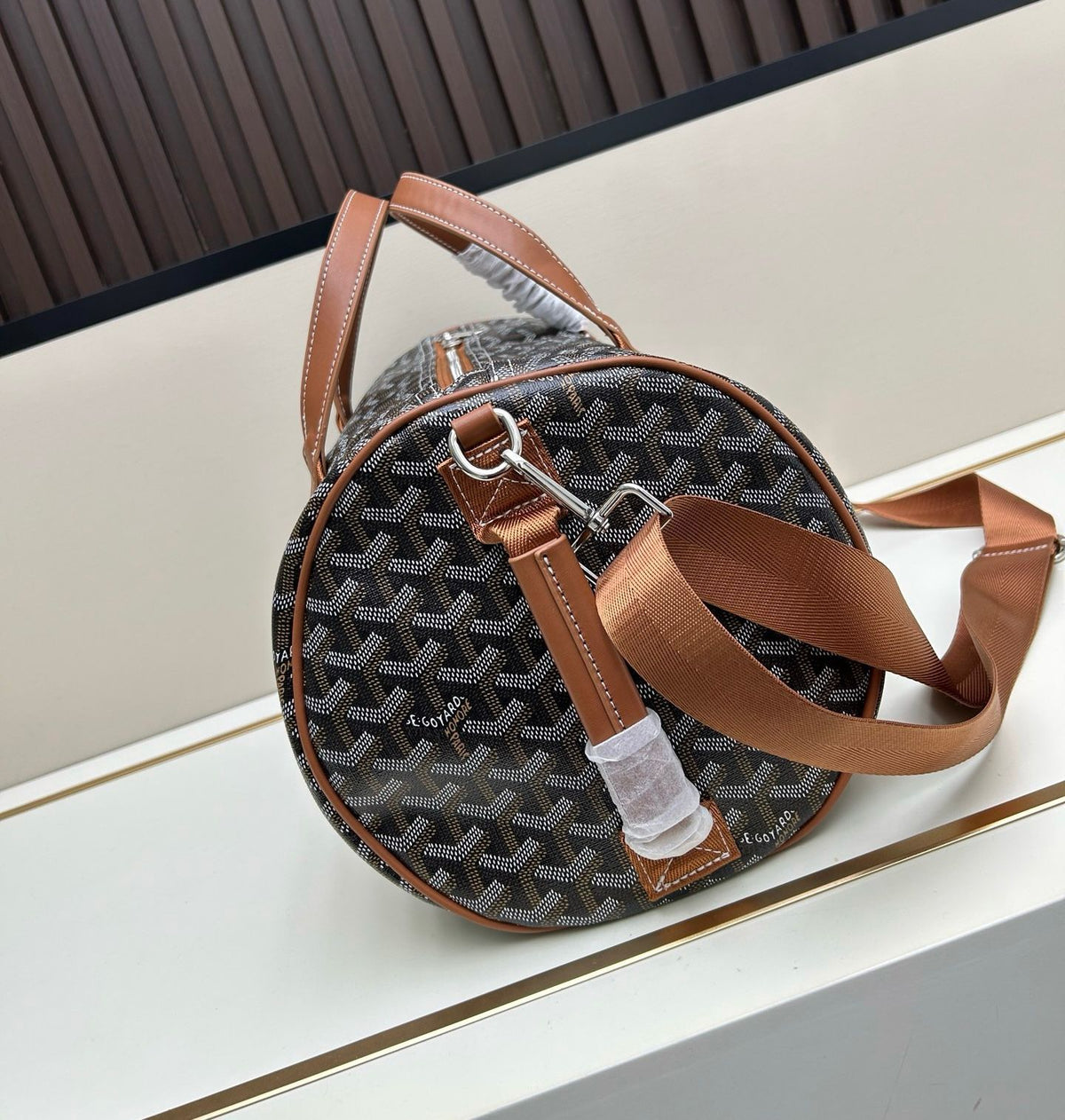 Side circular view of Goyardine canvas cylinder bag with attached leather strap