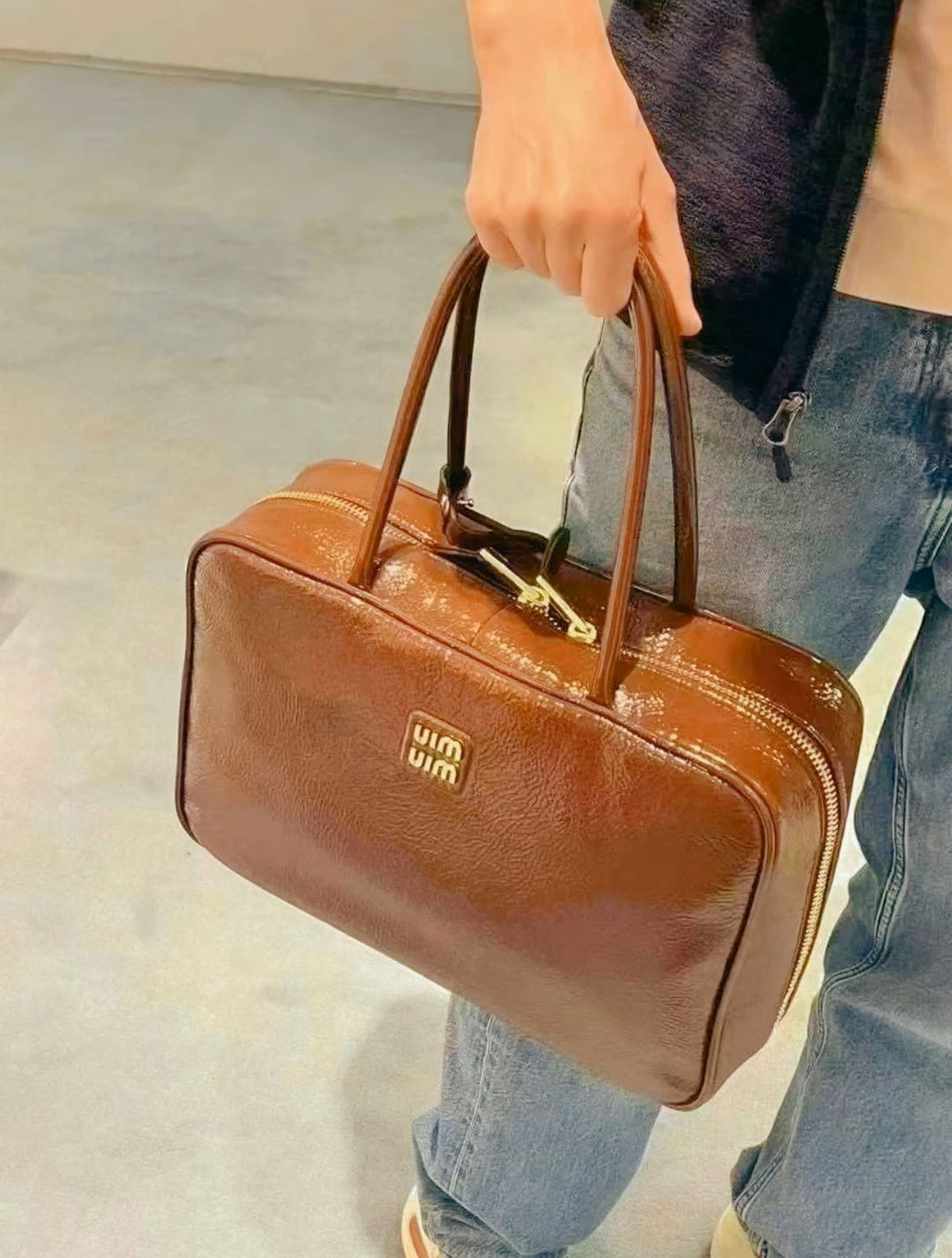 Person holding cognac brown Miu Miu leather top handle bag with jeans